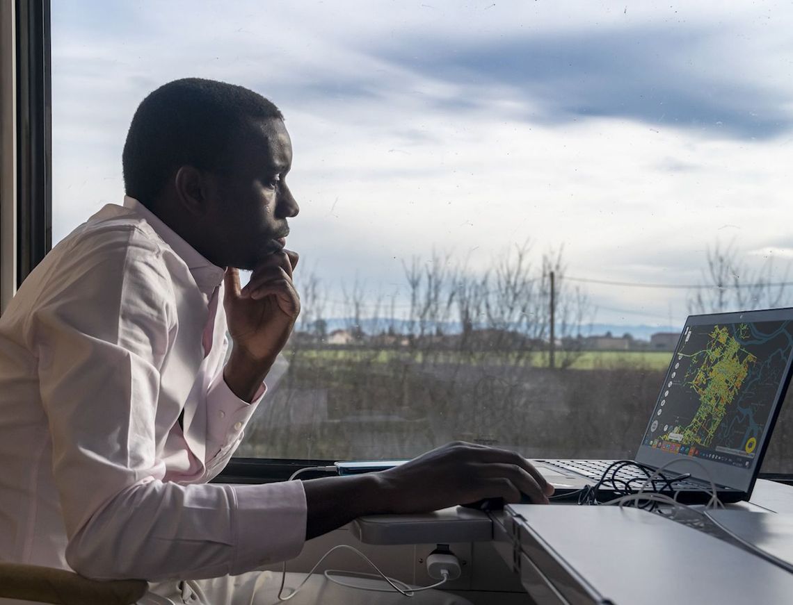 data strategist, assis dans un train, observant sur son ordinateur un plan de ville.